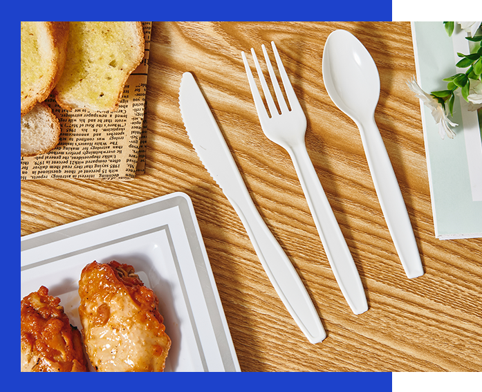 A wooden table featuring Jolly Chef white plastic cutlery: a knife, fork, and spoon, alongside a plate of fried chicken and slices of bread.