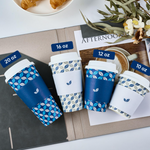 Four Jolly Chef coffee cups of varying sizes (10 oz to 20 oz) on a table with croissants, floral accents, and a magazine.