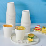 A stack of white disposable Jolly Chef cups beside a plate with colorful cakes, featuring a drink garnished with lime slices and ice cubes.