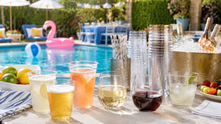 Plastic drinkware with cocktails, wine, and beer set beside a summer pool party drink station