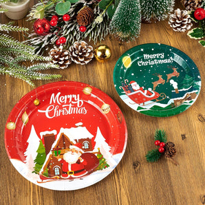 Two festive Christmas plates: a red one featuring Santa at a cozy cabin, and a green one with Santa's sleigh and reindeer, surrounded by holiday decor.