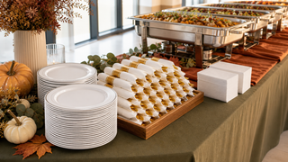 Fall catering buffet setup with white silver-rim plates, pre-rolled gold cutlery, and white napkins