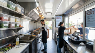 Staff cooking and serving a customer inside a clean, modern food truck during its grand opening