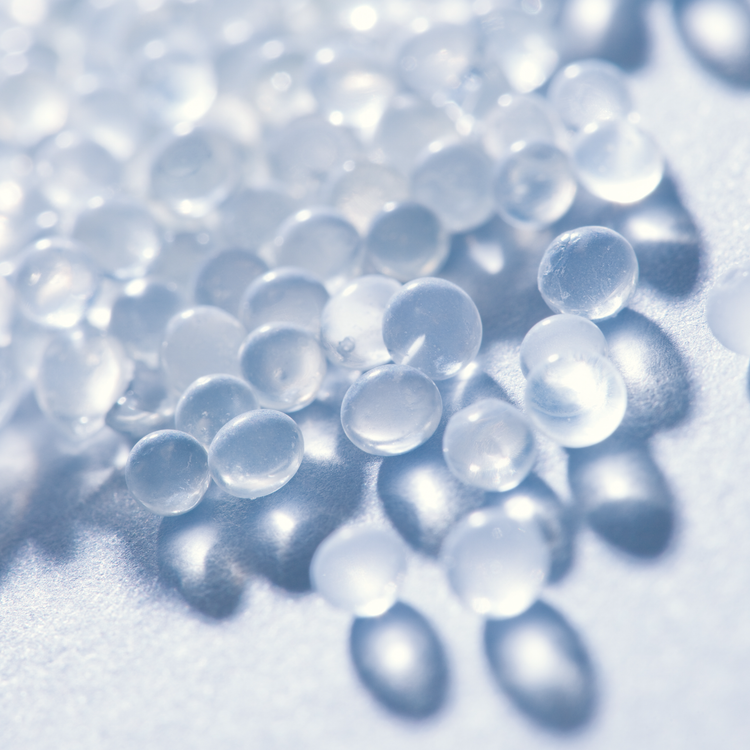 Jolly Chef Plastic Tableware Collection Main Image that is close-up of clear, glossy beads scattered on a light surface, casting soft shadows, showcasing their smooth texture and translucency. 