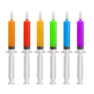 Six colorfully Jolly Chef filled syringes in orange, red, yellow, green, blue, and purple sit in a line against a white background.