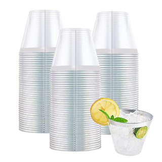 A stack of Jolly Chef Gold&Rose&Silver Rim Plastic(PS) Cups beside a filled glass of ice water garnished with lemon and mint leaves.