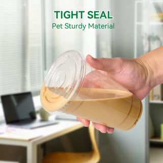 A hand holds a clear cup filled with iced coffee, showcasing its tight seal and sturdy material, against a modern office background.