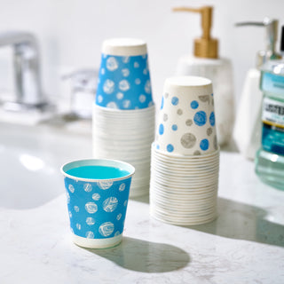 A JOLLY CHEF 5 oz Paper Cups with a patterned design holds bright blue liquid, surrounded by stacks of patterned cups and bathroom products.