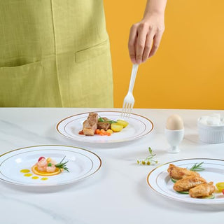 A hand holds a fork over a gourmet meal, chicken, vegetables, and a soft-boiled egg on Jolly Chef Gold&Silver Rim Plastic(PS) Plates.