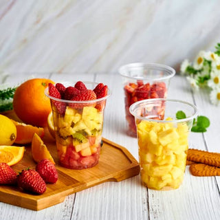 Clear PET cups filled with strawberry, pineapple, and kiwi fruit salad. Fresh fruit and biscuits surround the cups.
