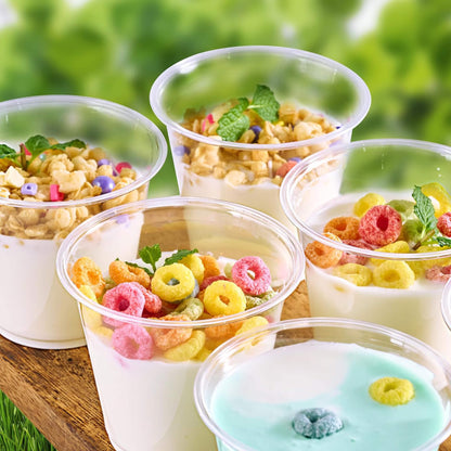 Colorful dessert cups filled with yogurt, granola, and fruity cereal, garnished with mint leaves, set against a blurred green background.