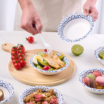 A hand with a fork picks up chicken from a colorful salad in a patterned plate, surrounded by fresh tomatoes, lime, and desserts.