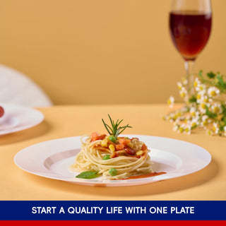 A Jolly Chef Disposable Heavy Duty Plastic Plate of spaghetti topped with vegetables and herbs, accompanied by a glass of red wine and flowers, against a warm backdrop.