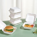 White sugarcane to-go boxes holding burgers and pasta, with stackable design.