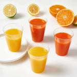 Four clear plastic cups filled with juice, two orange and two yellow, with citrus fruits sliced around them.