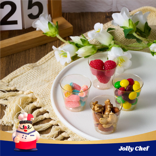 Colorful candies and nuts are displayed in clear Jolly Chef plastic cups on a white plate, surrounded by flowers and a decorative background.