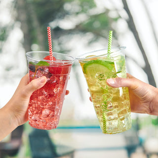 Two clear PET plastic cups with cold drinks: strawberry and lime. Disposable cups with patterned straws.