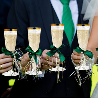 Four Jolly Chef 4.5oz Clear Gold Rim Champagne Flutes with golden rims and green ribbons, held by elegantly dressed guests at a celebration.