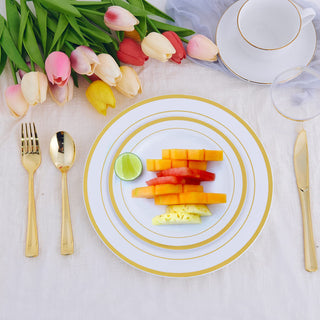 Elegant table setting with gold flatware, white plates, and fresh fruit salad with tulips.