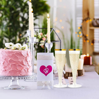 A pink frosted cake, two Jolly Chef 4.5oz Clear Gold Rim Champagne Flutes, and decorative candles set a romantic atmosphere for a celebration.