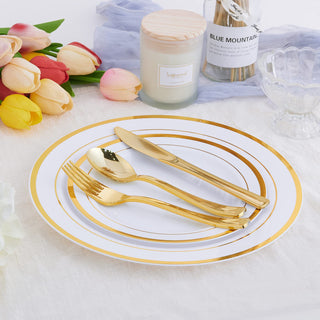 Elegant gold plastic cutlery on white plates with gold trim, beside tulips and a candle.