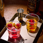 Clear dual-chamber 4.5oz Jager Bomb cups with red liqueur and orange-raspberry garnish on tray.