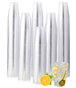 A stack of Jolly Chef Clear Plastic(PS) Cups with a refreshing glass of ice water garnished with lemon and mint in front, showcasing summer vibes.
