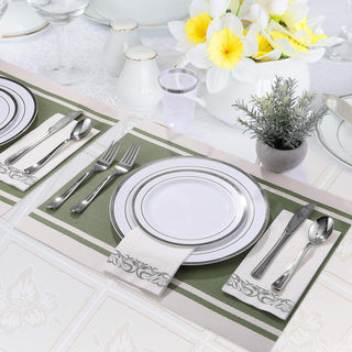 Elegant tablescape with white and silver plates, silverware, and a floral centerpiece on a green and white runner.