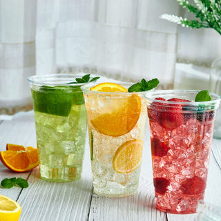 Three clear PET plastic cups filled with iced beverages: lime, orange-lemon, and berry, garnished with mint.