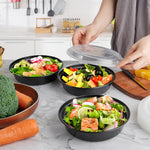 24oz black round meal prep containers filled with salads and ingredients, with a hand placing a lid on one.