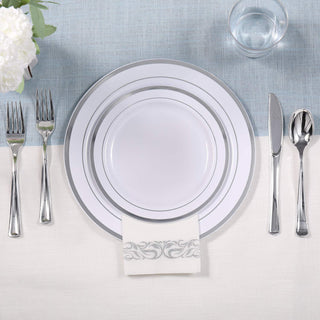Elegant white and silver place setting with plates, cutlery, napkin, and water glass on a blue and white tablecloth.