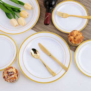 Elegant white and gold plastic plates with cutlery, wine, and cupcakes for a party setting.