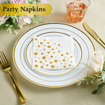 White 3-ply cocktail napkins with gold polka dots on a gold-rimmed plate, with gold cutlery & drink.