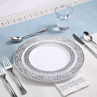Elegant white and silver disposable dinnerware set with plate, cutlery, glass, and napkin on a table setting.