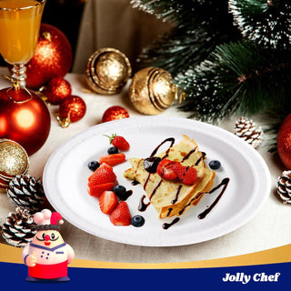White paper plate with crepes, strawberries, blueberries, and chocolate drizzle, with festive Christmas decor.