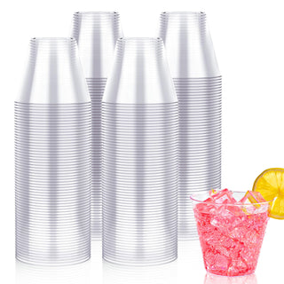 A stack of clear plastic cups beside a bright pink drink with ice and a lemon slice, against a white background.