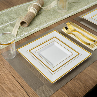 Elegant table setting with square white and gold plates, gold cutlery, and a woven placemat.