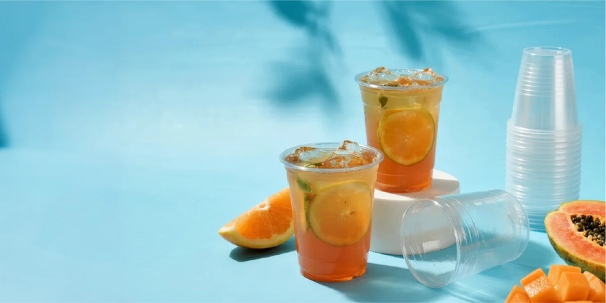 Refreshing fruit drinks with citrus slices, papaya, and empty plastic cups on a blue background.