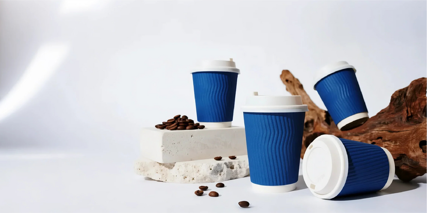 Blue coffee cups with lids, coffee beans, and driftwood on a white surface