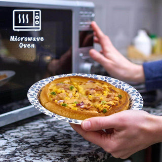 A person holds a jolly chef plate with a pizza near a microwave, preparing to heat it up. The kitchen countertop is visible in the background.