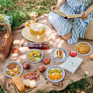 A cozy picnic setup with jolly chef plates of gourmet food, a wine bottle, and a book, surrounded by fresh peaches and a straw hat.
