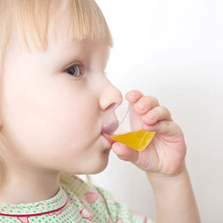 A child holds a small beaker filled with bright yellow liquid, wearing a patterned shirt with hearts and circles.